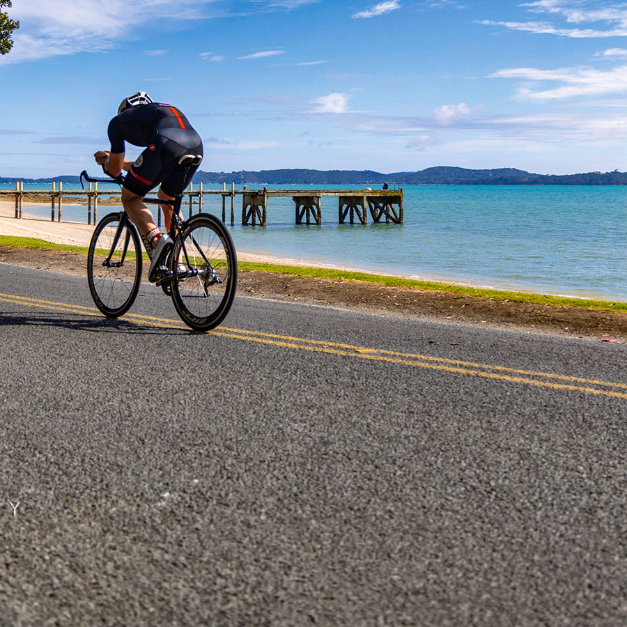 A triathlete cycling beside Maraetai Beach and its wharf