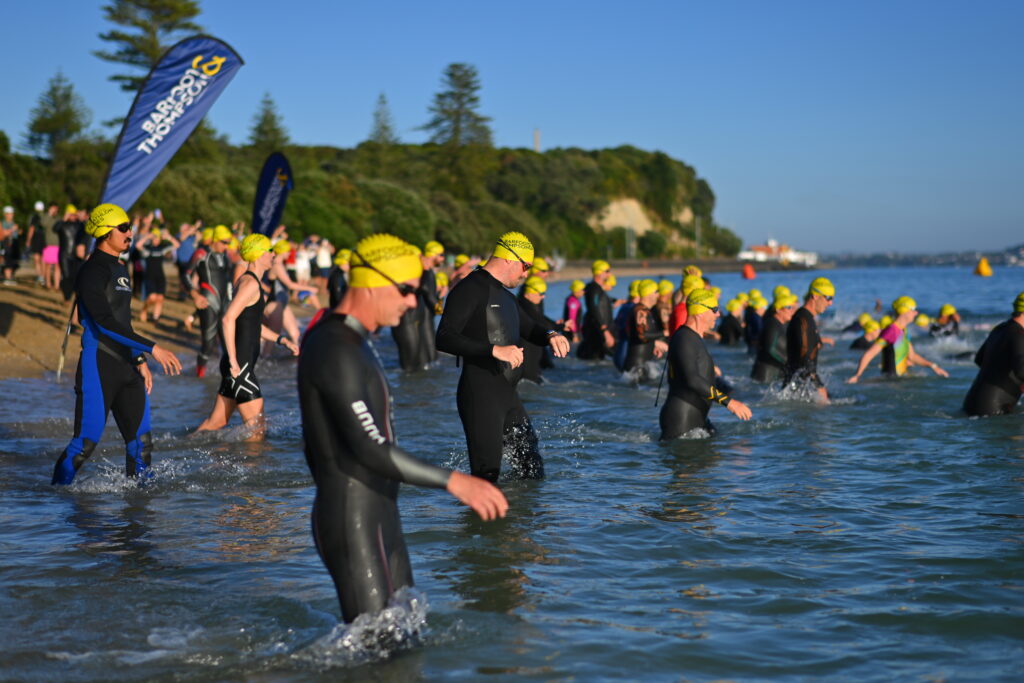 Athletes in yellow swim caps walk into the sea at the People's Triathlon swim start at Mission Bay.