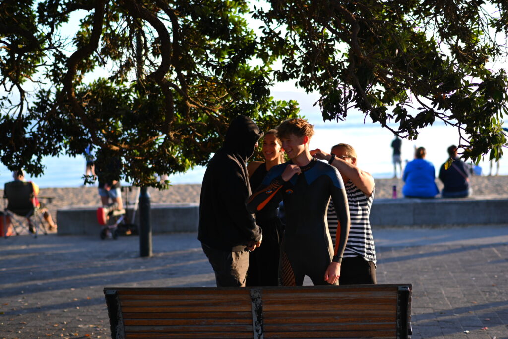 Athletes help each other prepare their wetsuits beside the beach before People's Triathlon.